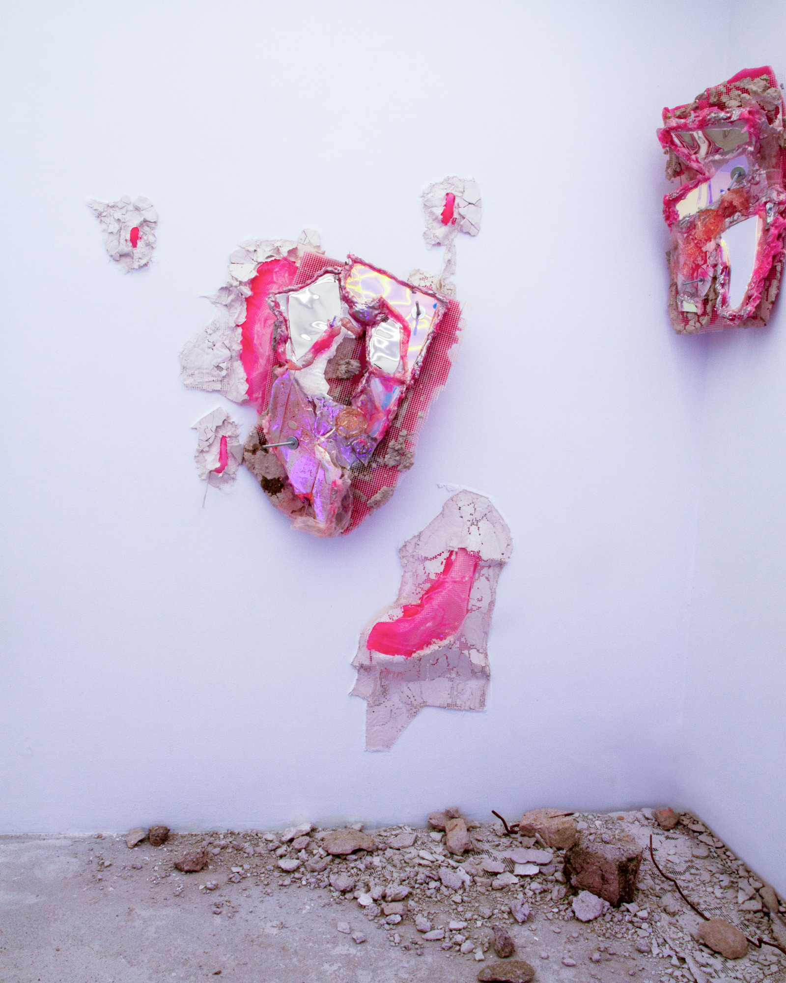 Gallery corner with two wall sculptures and loose rubble scattered on the floor